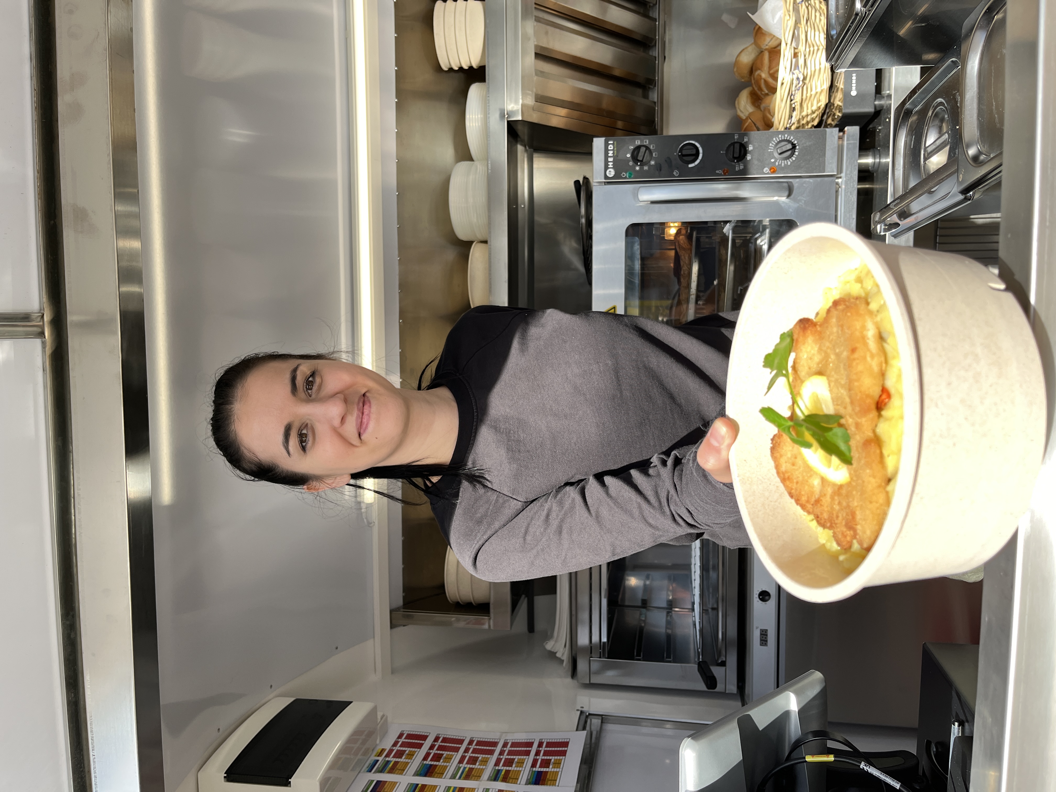 Eine Frau hält einen Mehrwegbehälter mit Schnitzel und Kartoffelsalat und lächelt in die Kamera